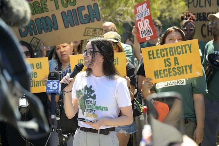 People stand in a group holding signs saying 'electricity is a necessity.'